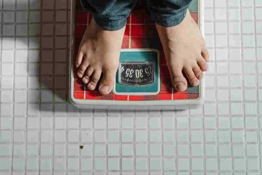 Man checking his weight on a scale, symbolizing myths about masturbation and weight loss.